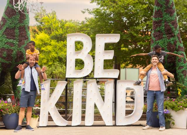 Family laughing in front of Be Kind sign at Elsewhere Garden Bar & Kitchen