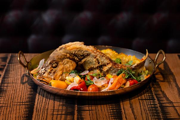 Plate of fish and vegetables served on wood tabletop.