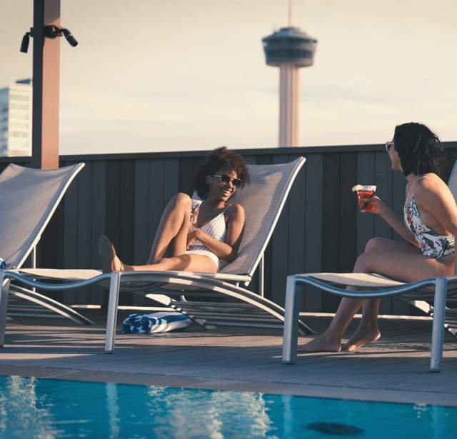 Two girls talking poolside on lounge chairs