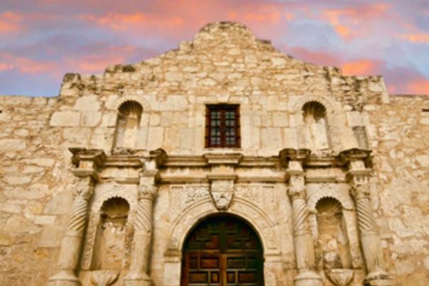 Front view of Alamo facade with light pink sky in background.
